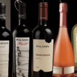 Display of Paladin Wines including Draggo Rosso Merlot and Prosecco Rosé, arranged on rustic wooden shelving in a warm-toned wine cellar setting